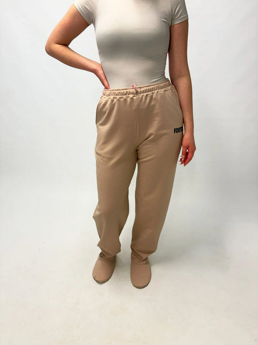 Model wearing beige FOOTED pants standing on a white background.