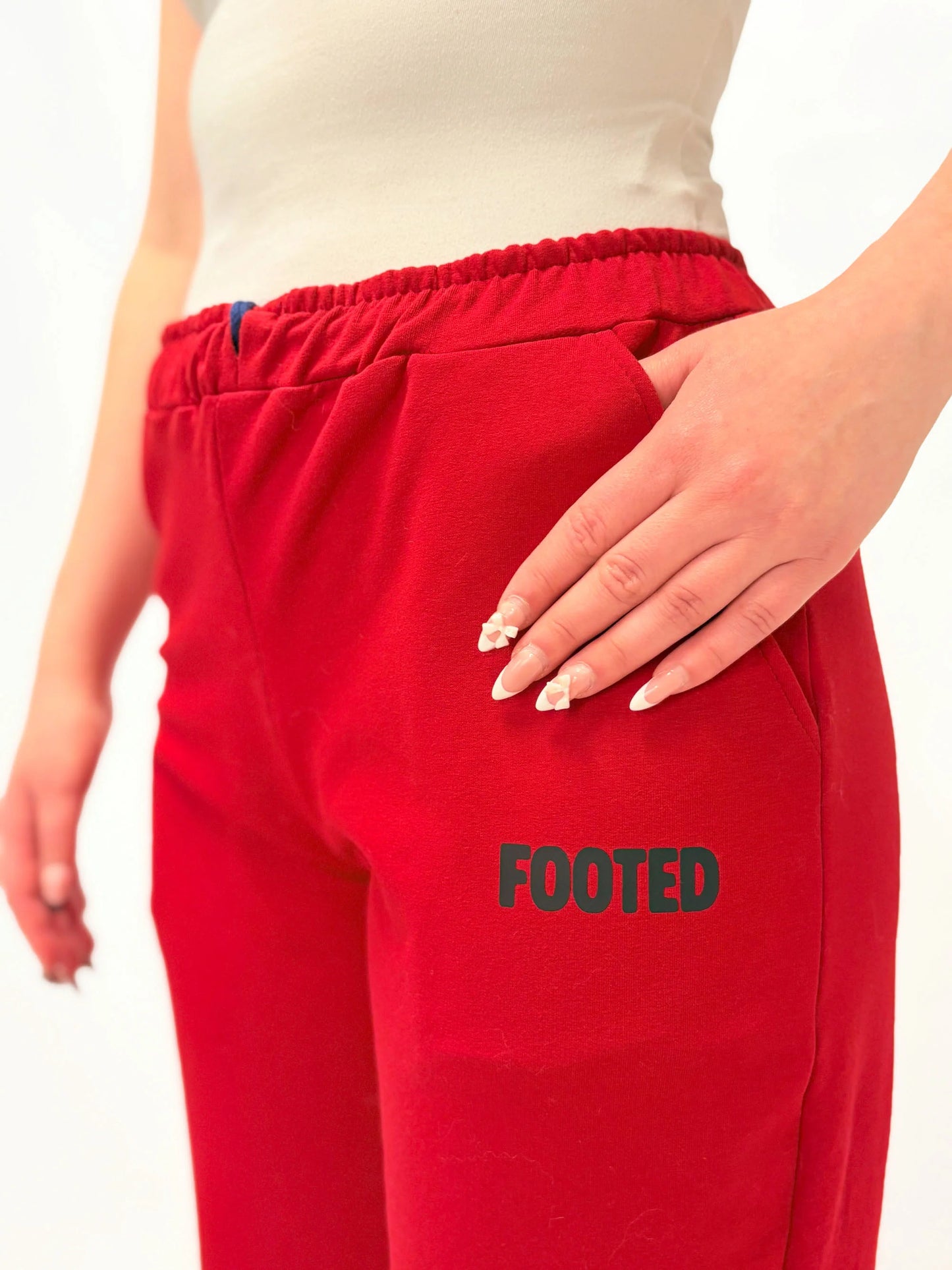 Close-up of red FOOTED pants showing the logo and fabric texture on a white background.