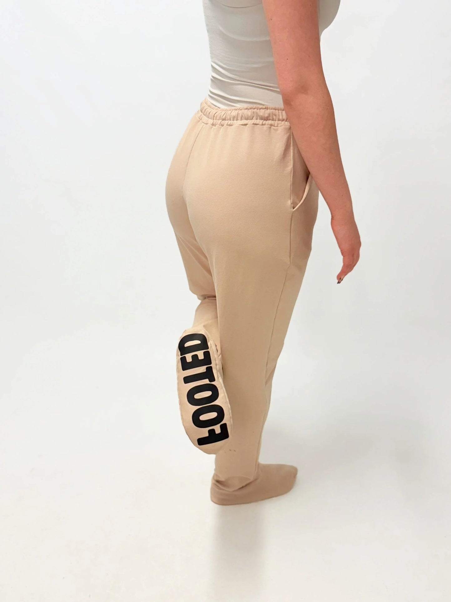 Model wearing beige FOOTED pants viewed from the back on a white background.