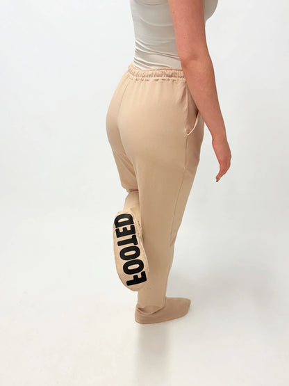 Model wearing beige FOOTED pants viewed from the back on a white background.