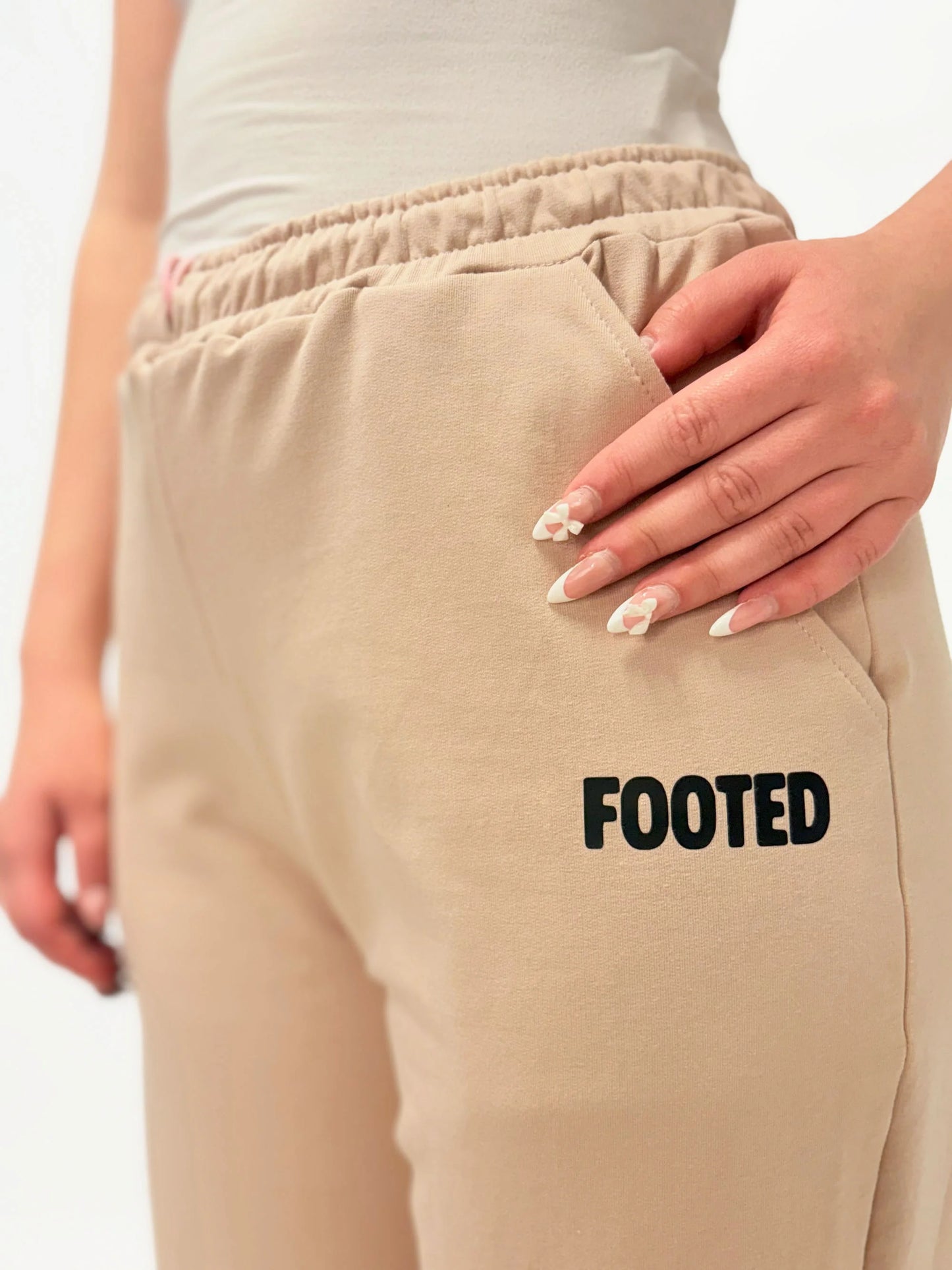 Close-up of beige FOOTED pants with logo near the pocket on a white background.