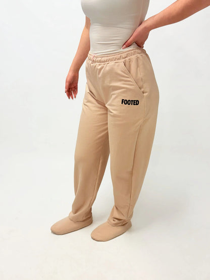 Model wearing beige FOOTED pants viewed from the side on a white background.