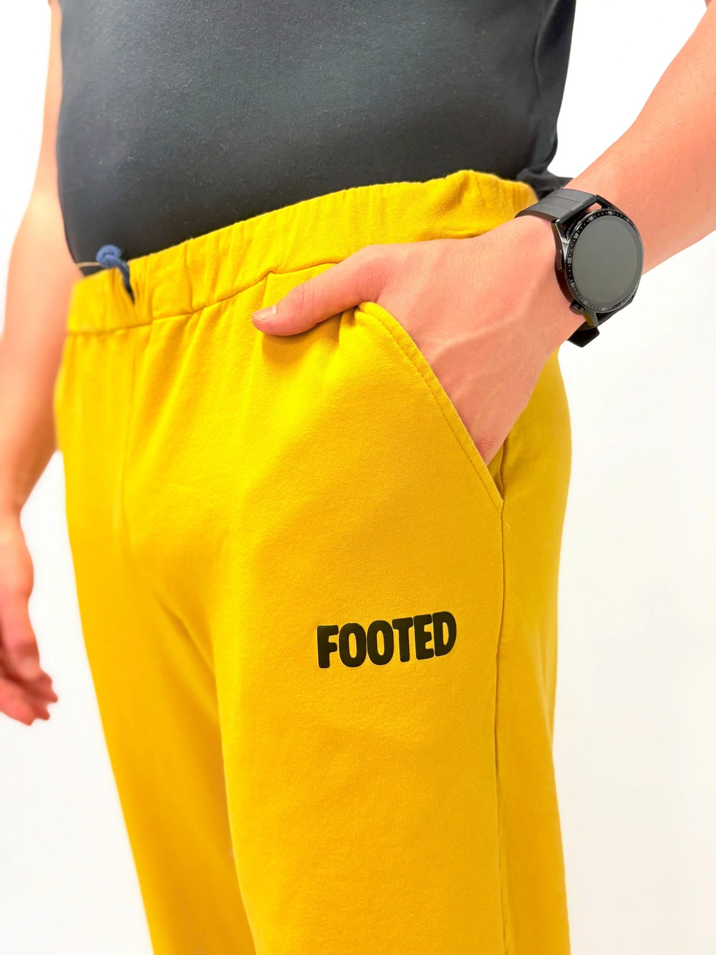 Close-up of yellow FOOTED pants showing pocket and logo on a white background.