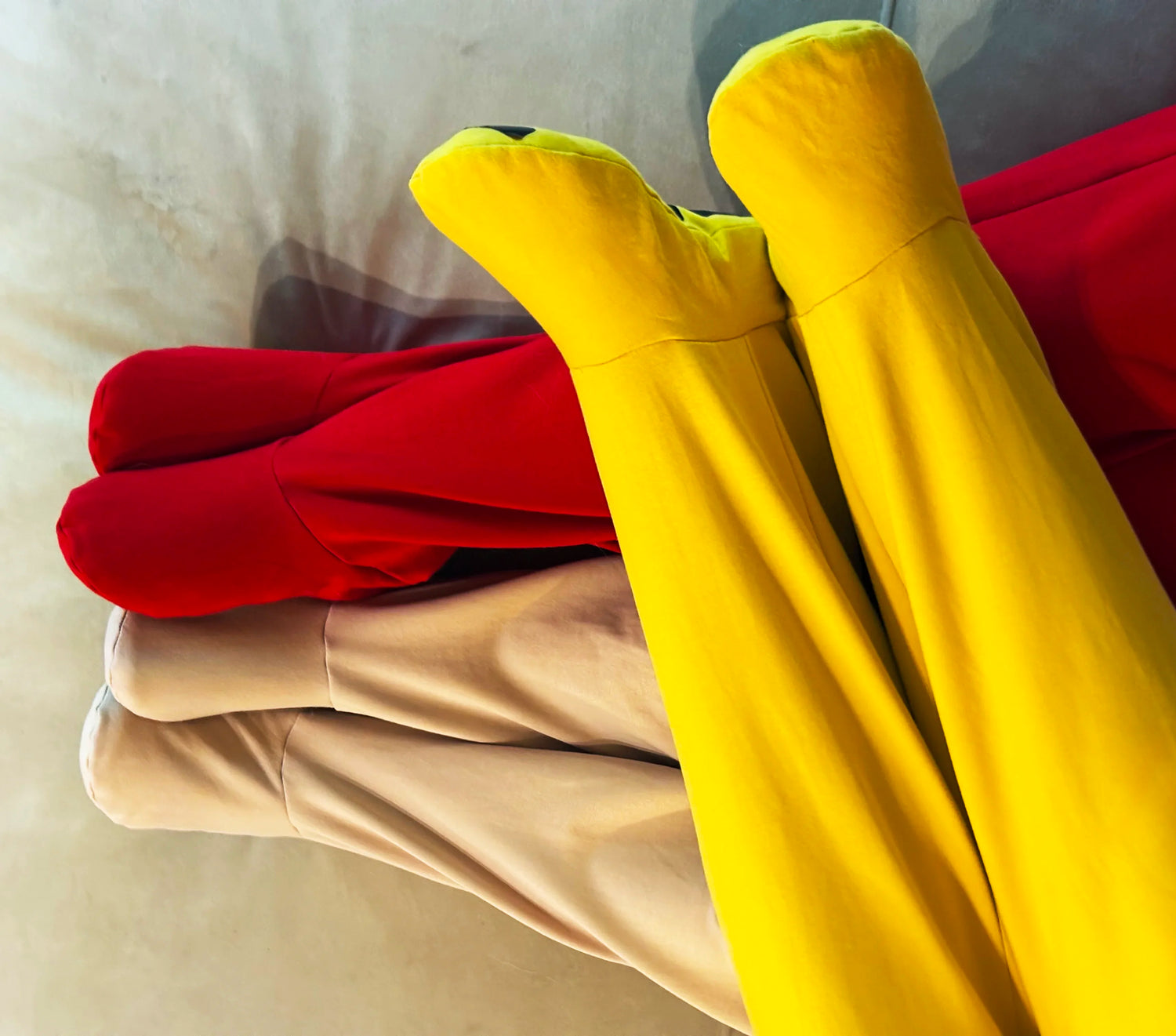 Yellow, red and beige FOOTED pants stacked together on a soft surface.