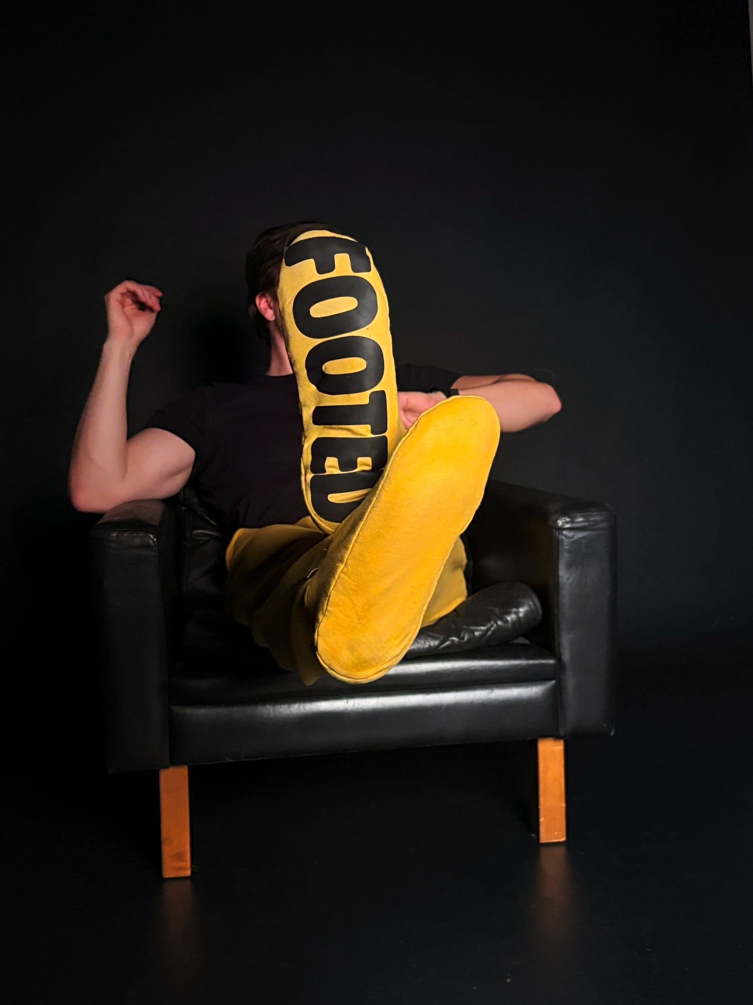 Person relaxing on a black chair wearing yellow FOOTED pants against a dark background.